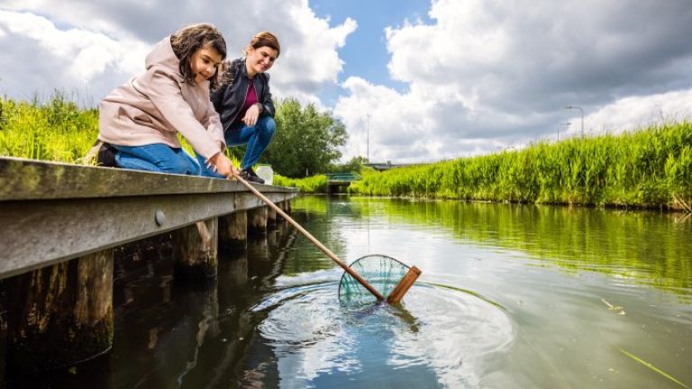 Vrouw en meisje op een steiger vissen met schepnet in het water