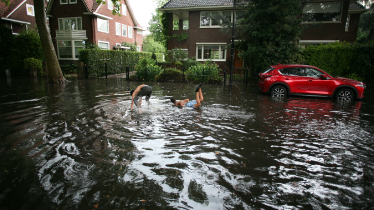 Kinderen hebben spetterplezier in een ondergelopen straat na hoosbui